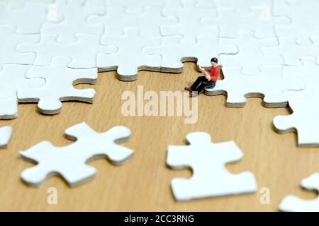 Foto concettuale strategia aziendale - giovani in miniatura seduti puzzle pezzo durante la lettura Foto Stock