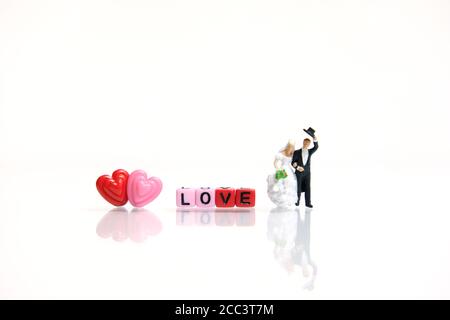 Fotografia in miniatura di persone per giorno di valentine, sposa e sposo con forma del cuore e perle di parole d'amore su sfondo bianco lucido Foto Stock
