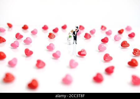 Fotografia di persone in miniatura. Sposa e sposo con forma a cuore e perle di parole d'amore su sfondo bianco lucido Foto Stock