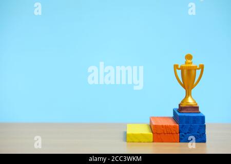 Trofeo d'oro in piedi sul colorato podio su un tavolo di legno Foto Stock