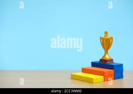 Trofeo d'oro in piedi sul colorato podio su un tavolo di legno Foto Stock