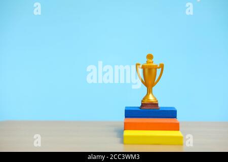 Trofeo d'oro in piedi sul colorato podio su un tavolo di legno Foto Stock