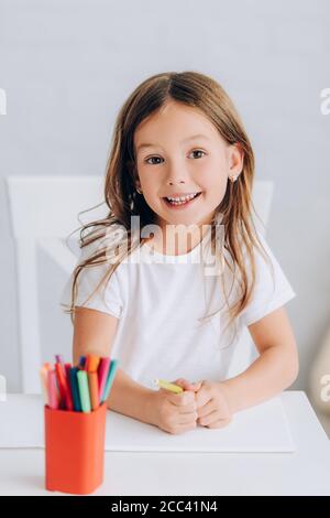 fuoco selettivo della ragazza eccitata in t-shirt bianca che tiene il feltro penna e guardando la fotocamera Foto Stock