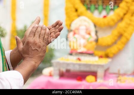 Primo piano di mani anziane che offrono Bhajan o inno Di fronte al Signore Ganesha Idol aggrappando durante Ganesha O vinayaka Chaturthi festivale cerimonia Foto Stock