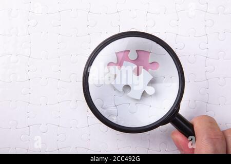 Mano che tiene una lente d'ingrandimento su un puzzle bianco Foto Stock