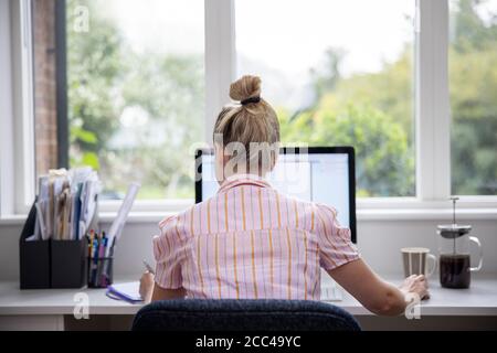 Vista posteriore di Donna che lavora da casa su computer in Ufficio domestico Foto Stock