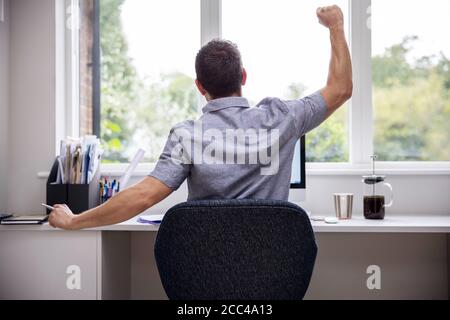 Vista posteriore dell'uomo che lavora da casa su computer in Home Office stretching alla scrivania Foto Stock