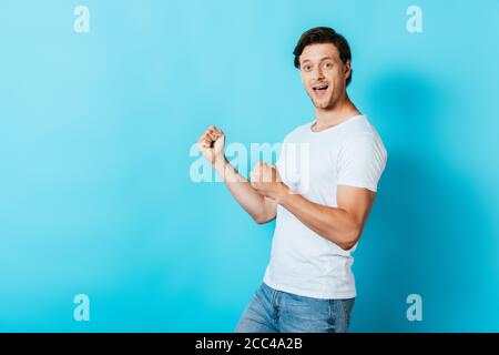 Uomo che guarda la fotocamera mentre mostra il gesto di sì su blu sfondo Foto Stock