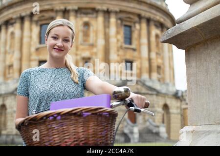 Ritratto di studentessa cavalcare bicicletta vecchio stile intorno Oxford University College Buildings di Radcliffe Camera in Radcliffe Square UK Foto Stock