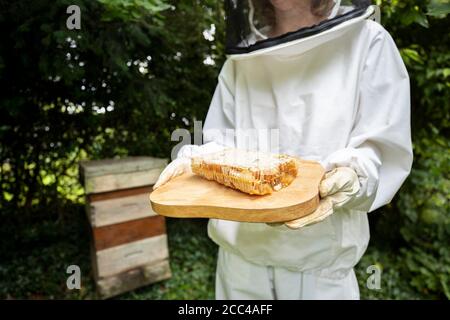 Beekeper femminile in indumenti protettivi fuori Honey Bee Hive Holding Nido d'ape Foto Stock