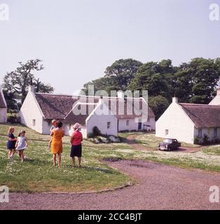 Anni '60, immagine storica di questa epoca che mostra due donne con i loro bambini in piedi fuori del grazioso, tradizionale a un piano, vecchi cottage in pietra dipinta di bianco presso il villaggio di Swanston, Edimburgo, Scozia. Foto Stock