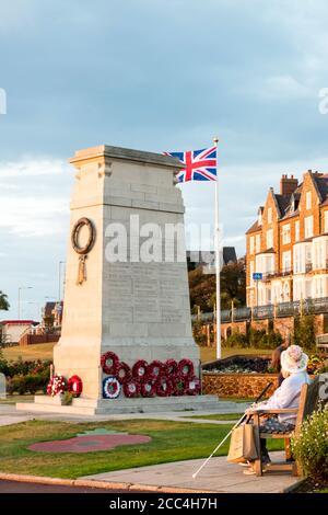 Persone che siedono accanto al memoriale di guerra di Hunstanton con una bandiera di Union Jack. Foto Stock