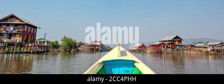 Barca che arriva in un colorato villaggio galleggiante con palafitte in Birmania, Myanmar Foto Stock