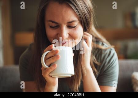 Primo piano di una bella donna caucasica brunette che gusta il caffè tazza a casa Foto Stock
