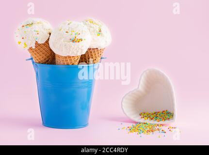 Coni di gelato in un secchio blu e piatto bianco in forma un cuore con la parte superiore su sfondo rosa. Un cono gelato in stile wafer. Foto Stock