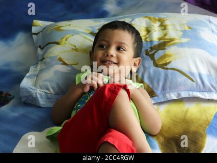 2 anni sorridente simpatico bambino asiatico sdraiato sul letto, guardando la madre e riposandosi Foto Stock