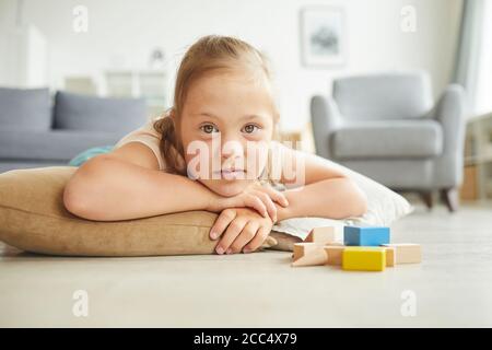 Ritratto di ragazza con sindrome di Down sdraiata sul pavimento con i giocattoli e guardando la fotocamera Foto Stock