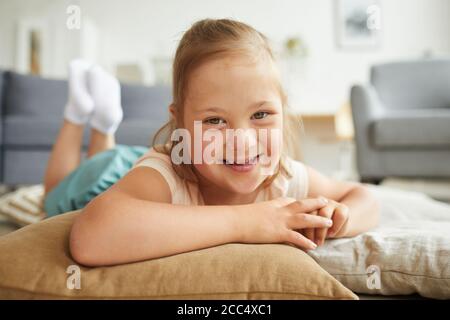 Ritratto di bambina con sindrome di Down sorridente a macchina fotografica mentre sdraiato su cuscini sul pavimento Foto Stock