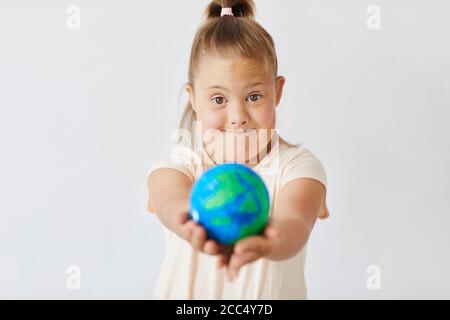 Ritratto della sindrome di Down ragazza tenendo modello della Terra pianeta e guardando la telecamera isolata su sfondo bianco Foto Stock