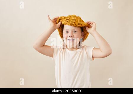 Ritratto di ragazza con sindrome Down indossare cappello di lana sorridente sulla fotocamera contro lo sfondo bianco Foto Stock
