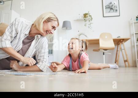 Giovane donna sorridente che ride con sua figlia mentre si sdraiano sul pavimento e la raccolta di puzzle a casa Foto Stock