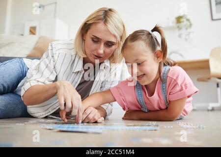 Madre insegnando sua figlia con sindrome giù raccogliendo i puzzle loro sdraiato sul pavimento della camera Foto Stock