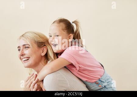 Madre felice che cavalca sua figlia con la sindrome di Down su di lei di nuovo sullo sfondo bianco Foto Stock