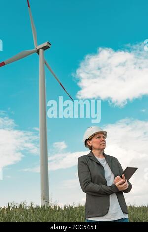 Ingegnere femminile con computer tablet in una moderna azienda agricola con turbine eoliche durante la pianificazione del progetto di manutenzione Foto Stock