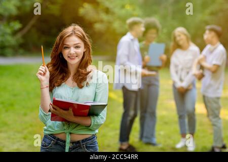 Concetto di istruzione. Bella studentessa nerdy e gruppo dei suoi compagni di classe all'aperto Foto Stock