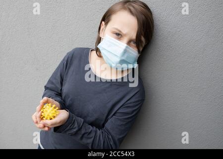 Ragazzo caucasico giovane che indossa una maschera chirurgica blu e tiene Un modello di virus corona durante la pandemia COVID-19 Foto Stock
