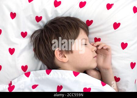 il ragazzo sta dormendo sonoramente su un letto bianco con cuori rossi. vista dall'alto Foto Stock
