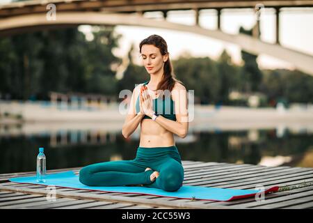 Donna sportiva meditando su piattaforma di legno Foto Stock