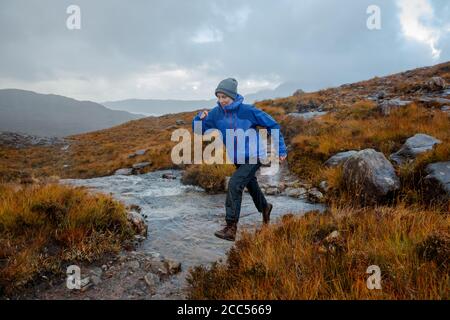 Una persona che cammina nella campagna scozzese vicino al Allt Coire Rooill fiume in Torridon, Scozia Foto Stock