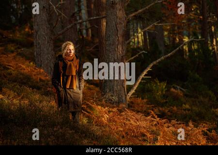Una donna che cammina in una foresta con un sacco di felci arancione Foto Stock