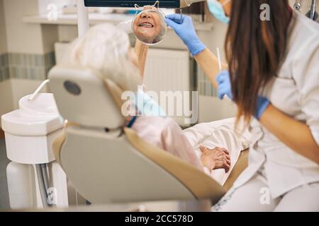 Dentista femminile che esamina i denti usando lo specchio in clinica dentale Foto Stock