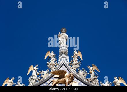 Particolare della statua centrale di cristo e degli angeli sulla facciata della Basilica di San Marco a Venezia che si affaccia su un cielo azzurro chiaro e estivo. Foto Stock