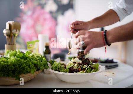 primo piano di mani, l'uomo mette la salsa in insalata, cibo sano, insalata verde, fuoco selettivo Foto Stock