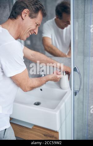 Felice uomo dai capelli corti che preme una bottiglia della pompa Foto Stock