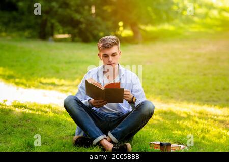 Tempo libero all'aperto. Giovane bel ragazzo che riposa con il libro nel parco Foto Stock