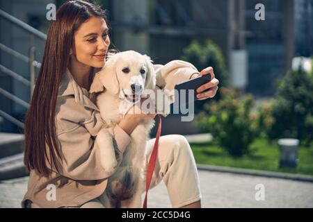 Donna sorridente che si fotografa con il suo cane fuori Foto Stock