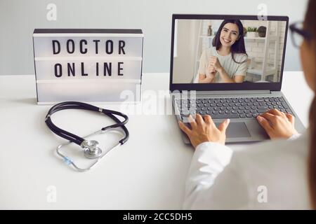 Medico online. Il paziente e il medico utilizzano un computer portatile per videochiamata online. Il medico consulta a distanza mentre si siede al tavolo nell'ufficio del Foto Stock