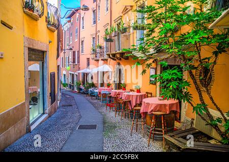 Desenzano del Garda, Italia, 11 settembre 2019: Tavoli da ristorante su botti e sedie in legno in tipica stradina italiana e tradizionali edifici colorati nel centro storico della città Foto Stock