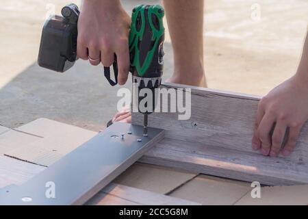 Assemblaggio mobili - viti di accesso per un tavolo in legno a testa battibile. Avvitatore elettrico nelle mani dei lavoratori Foto Stock