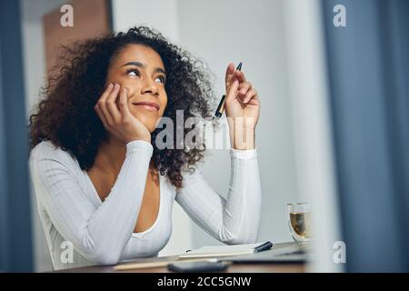 Donna attraente con capelli ricci pensando e guardando felice Foto Stock