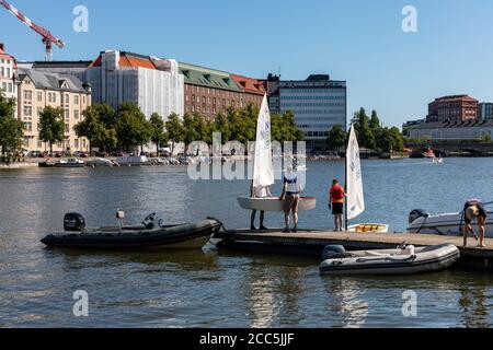 Uomini che trasportano un leggero skiff a vela su un molo a Kaisaniemi Bay a Helsinki, Finlandia Foto Stock