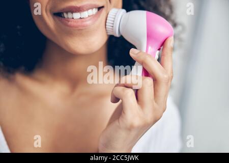 Gioioso giovane con capelli scuri che applica uno strumento di massaggio Foto Stock