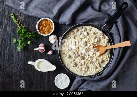 Funghi all'aglio cremosi, champignons saltati in salsa di panna acida in padella. Ingredienti su un tavolo di legno scuro, piatto, vista orizzontale da abov Foto Stock