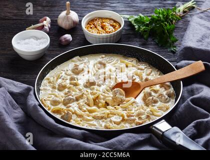 Primo piano di salsa di funghi cremosa a bottoni estremamente versatile, champignons saltati in salsa di panna acida in una padella su un tavolo di legno scuro con ingredienti Foto Stock