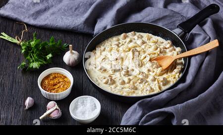 Salsa di funghi cremosa estremamente versatile, champignons saltati in salsa di panna acida in una padella, ingredienti su un tavolo di legno scuro, vi orizzontale Foto Stock