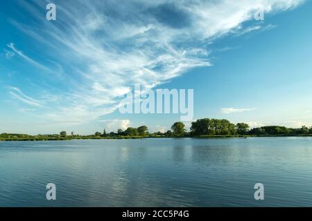 Nuvole bianche che soffiano nel cielo blu su un pacifico lago Foto Stock